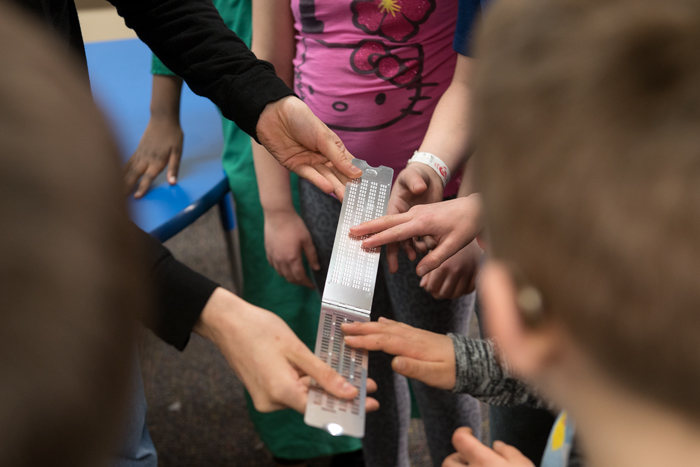 Teacher and students with hands on metal braille 