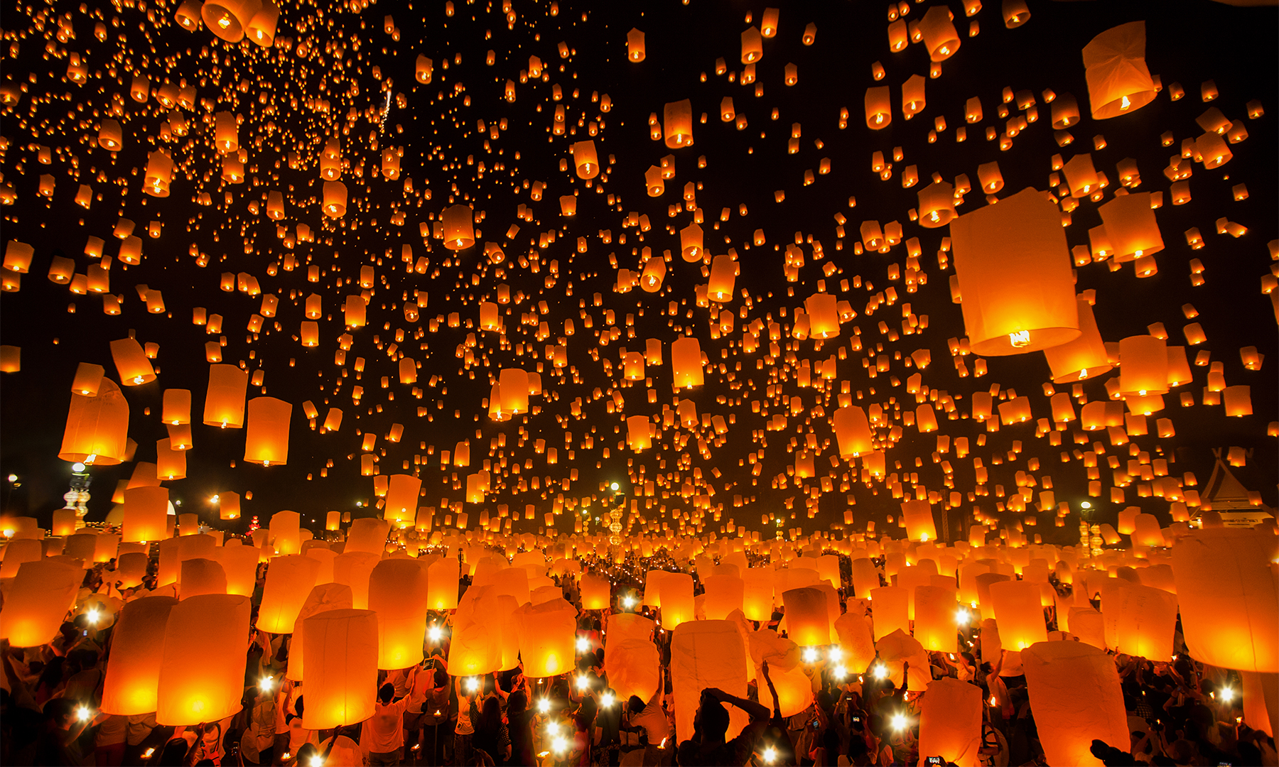 Flying wish lanterns being released against a night sky.