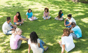 Young people sit in a circle on the grass.