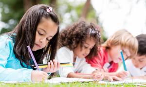 young students coloring lying on grass