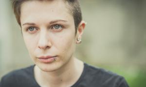 A teenager with piercings looks pensively off camera