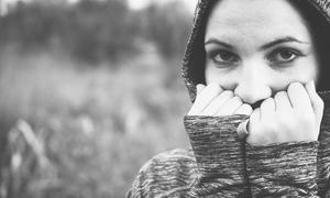 female student with hands over mouth and hood up in black and white