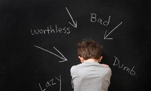 boy looking down shamefully from behind with words lazy worthless bad dumb written on chalkboard pointing to him