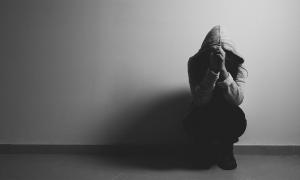 Distraught student sitting against wall with hoodie drawn