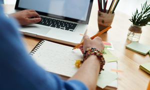 Person writing notes while looking at computer