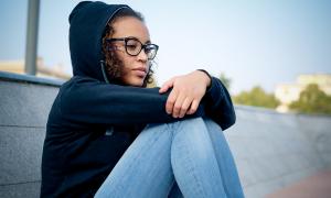 Female student with her knees pulled up, looking pensive.