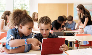 Two students sharing a tablet screen, one pointing to something on the screen.