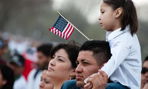 Young child holding American flag sitting on top of parent's shoulders.