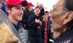 Young white student with "Make America Great Again" hat standing in front of elderly Native American man.