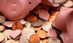 Shattered piggy bank laying on top of a large collection of U.S. currency coins.