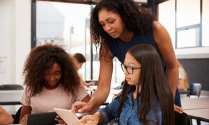 Teacher looking over a student's shoulder while pointing to something on their iPad.