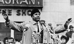Bayard Rustin at a podium with microphones, addressing a crowd.