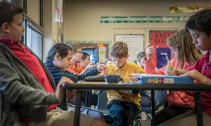 Young students sitting at tables, focused on assignments in front of them.