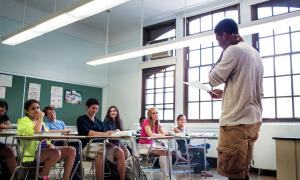 Student standing in front of classroom full of fellow students as they present something from a sheet of paper.