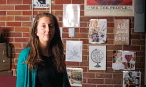 Alexandra Melnick sits in front of a brick wall with several posters hanging behind her.