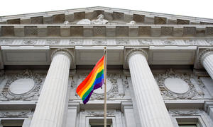 LGBTQ pride flag flying in front of courthouse-like building.