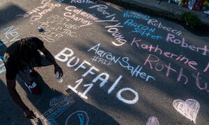 A teenager honors those who lost their lives in the Buffalo attack by writing their names in chalk on the street in front of a sidewalk memorial.