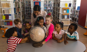 A group of young children in a school library with their teacher looking at a globe.