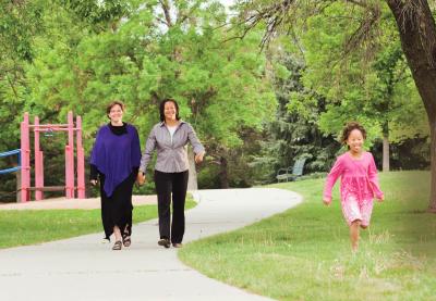 Photo of two adults holding hands while a happy child run at the park