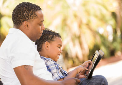 father and son looking at ipad outdoors