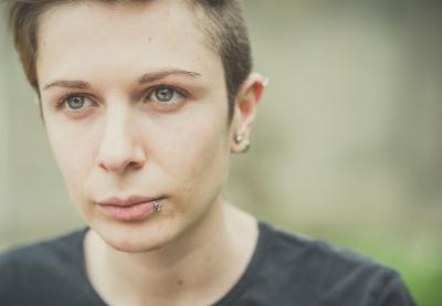 A teenager with piercings looks pensively off camera