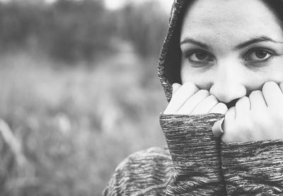 female student with hands over mouth and hood up in black and white