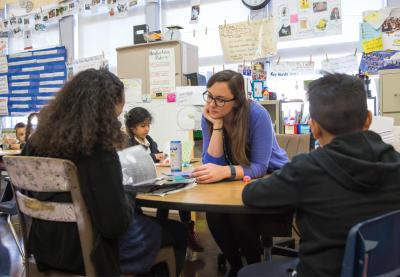 female teacher talking with students at desk