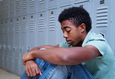 Sad African American student sitting against lockers | Hate at School May 2018 