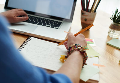 Person writing notes while looking at computer