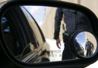 Police officer seen approaching in a car's side mirror.