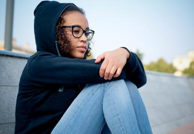 Female student with her knees pulled up, looking pensive.
