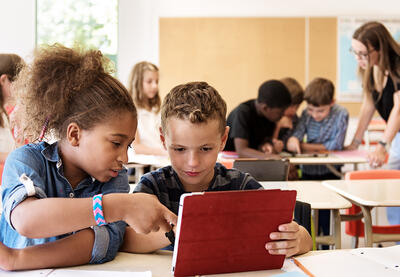 Two students sharing a tablet screen, one pointing to something on the screen.