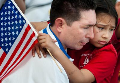 Young child holding American flag being held by adult.