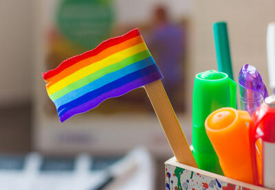 Small LGBTQ flag sitting in bin with writing utensils.