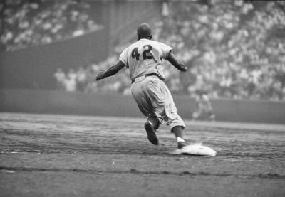 Jackie Robinson rounding first base at baseball game.