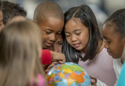 Several young kids gathered around a small globe, pointing at various spots.