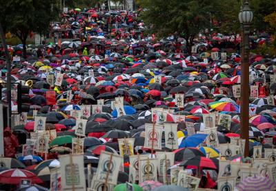 Hundreds of people gathered together, holding protest signs and umbrellas in Los Angeles, California.