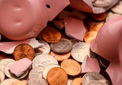 Shattered piggy bank laying on top of a large collection of U.S. currency coins.