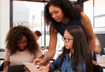 Teacher looking over a student's shoulder while pointing to something on their iPad.