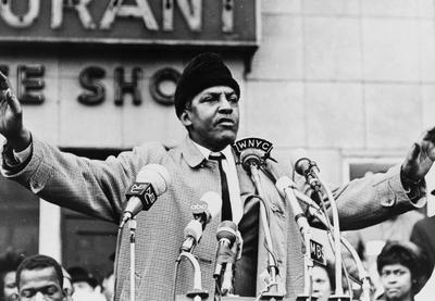 Bayard Rustin at a podium with microphones, addressing a crowd.