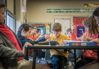 Young students sitting at tables, focused on assignments in front of them.