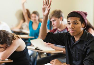 Young African-American teenager raising their hand in class.