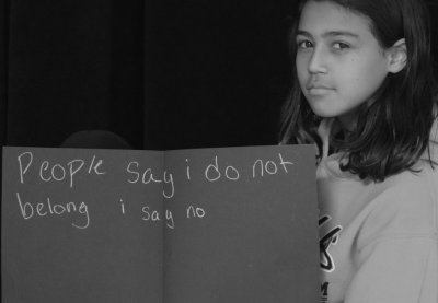 Young student holding sign that says "People say I do not belong I say no."