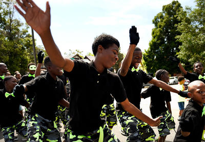 Young men of color in matching outfits dancing together outside.