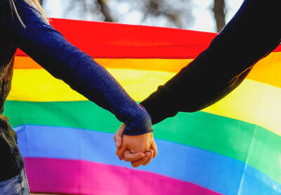 Two people holding hands in front of a rainbow flag.