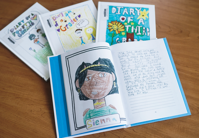 Several student-created books on a table, with the top one opened to a page featuring a drawing of a person of color named Sienna.