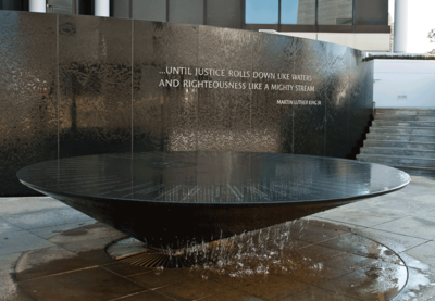 Photograph of the Civil Rights Memorial wall and fountain. The words "...until justice rolls down like waters and righteousness like a mighty stream. —Martin Luther King Jr." appear plainly on the wall.