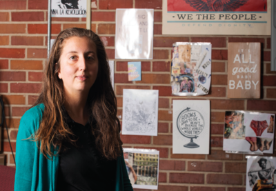Alexandra Melnick sits in front of a brick wall with several posters hanging behind her.