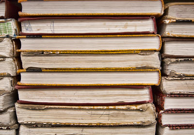 A stack of textbooks—viewed from the side—in varying conditions of use, from good to worn out.