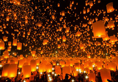Flying wish lanterns being released against a night sky.